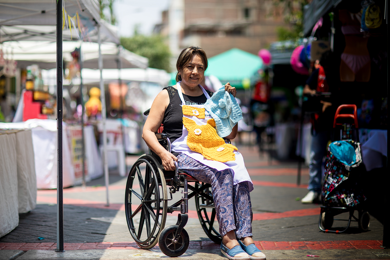 Mujer con discapacidad física, usuaria de silla de ruedas, presenta los productos de su emprendimiento en una feria.