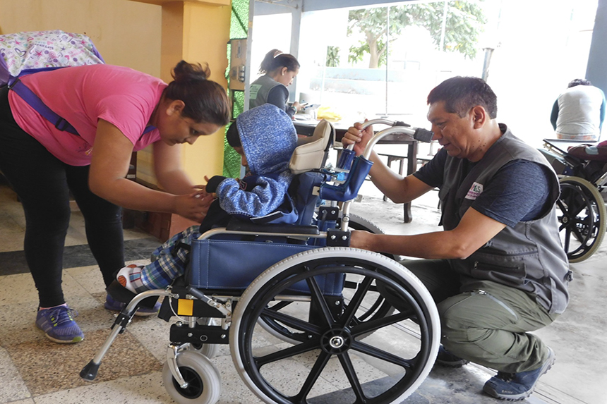 Niño en silla de ruedas recibe tecnología de apoyo de parte de dos personas.
