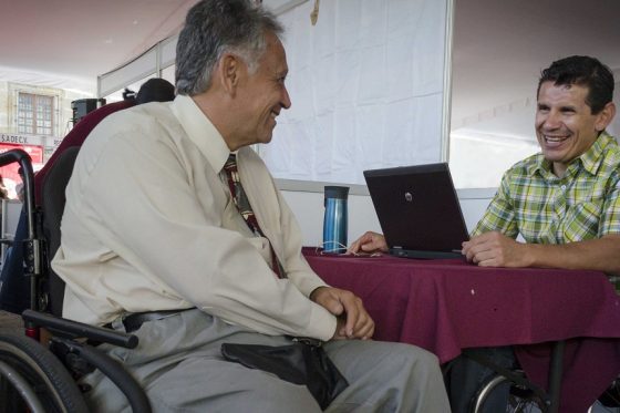 Dos personas usuarias de sillas de ruedas sonríen mutuamente