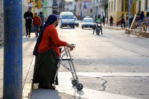 Una mujer adulta mayor con discapacidad física, usuaria de un andador, observa la calle antes de cruza.