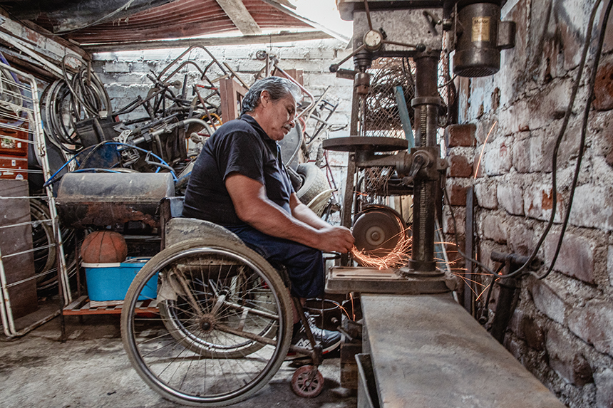 Una persona con discapacidad física usuario de silla de ruedas utiliza un esmeril de banco para realiza un trabajo en su taller.