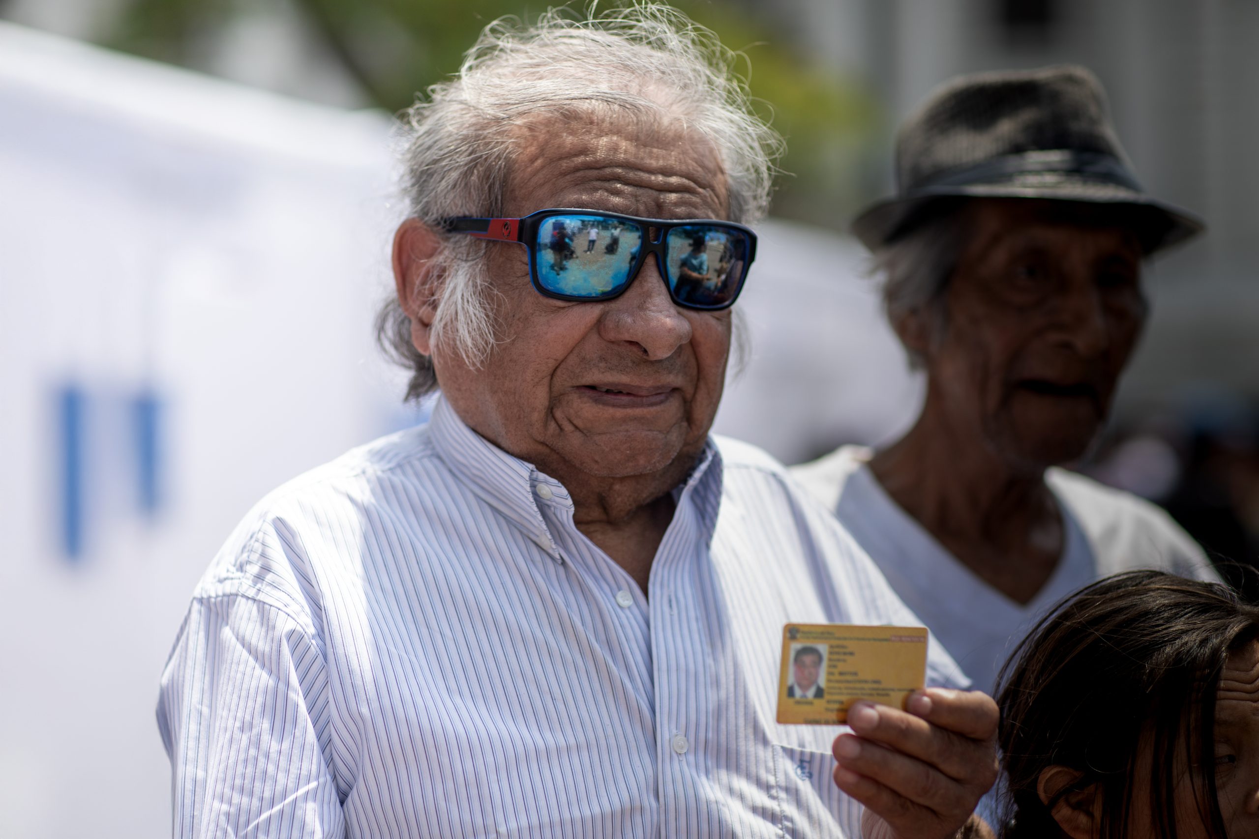 Un adulto mayor con discapacidad visual sostiene su carné de inscripción al Registro Nacional de la Persona con Discapacidad de color amarillo, lo que indica que tiene discapacidad severa.
