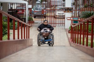 Una mujer adulta con discapacidad, usuaria de silla de ruedas, se desplaza y accede a un espacio utilizando una rampa.