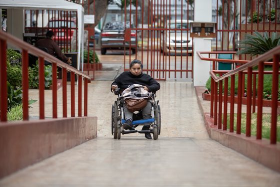 Una mujer adulta con discapacidad, usuaria de silla de ruedas, se desplaza y accede a un espacio utilizando una rampa.
