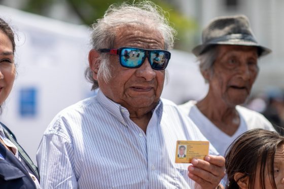 Un adulto mayor con discapacidad visual sostiene su carné de inscripción al Registro Nacional de la Persona con Discapacidad de color amarillo, lo que indica que tiene discapacidad severa.