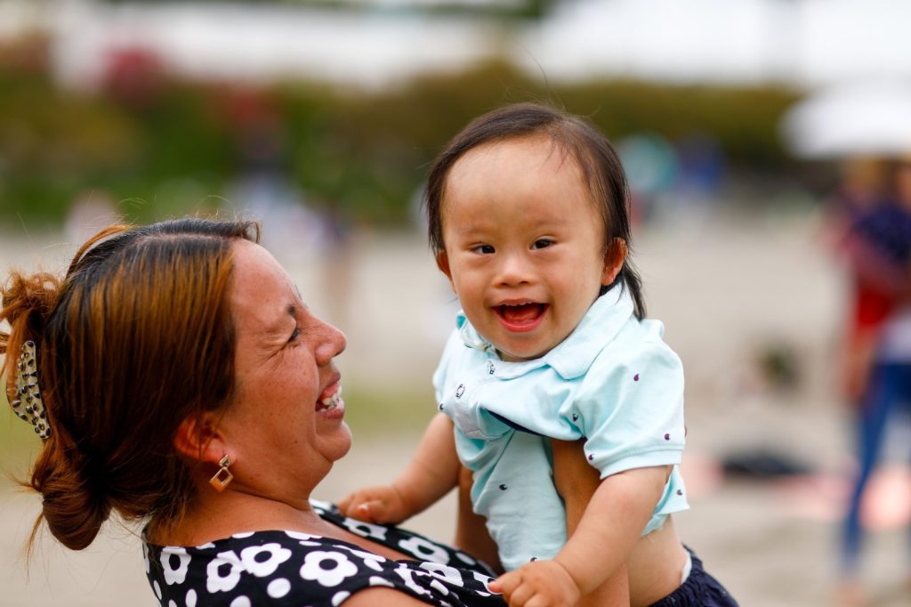 Mujer sonriente sostiene en brazos a un niño pequeño que también sonríe, en un ambiente al aire libre
