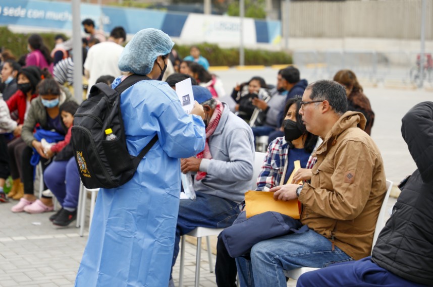 La imagen muestra a un personal de salud de espaldas atendiendo a un grupo de personas.