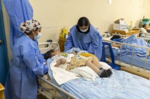 La imagen muestra a dos personas del ámbito de la salud acomodando a un niño en una camilla de hospital.