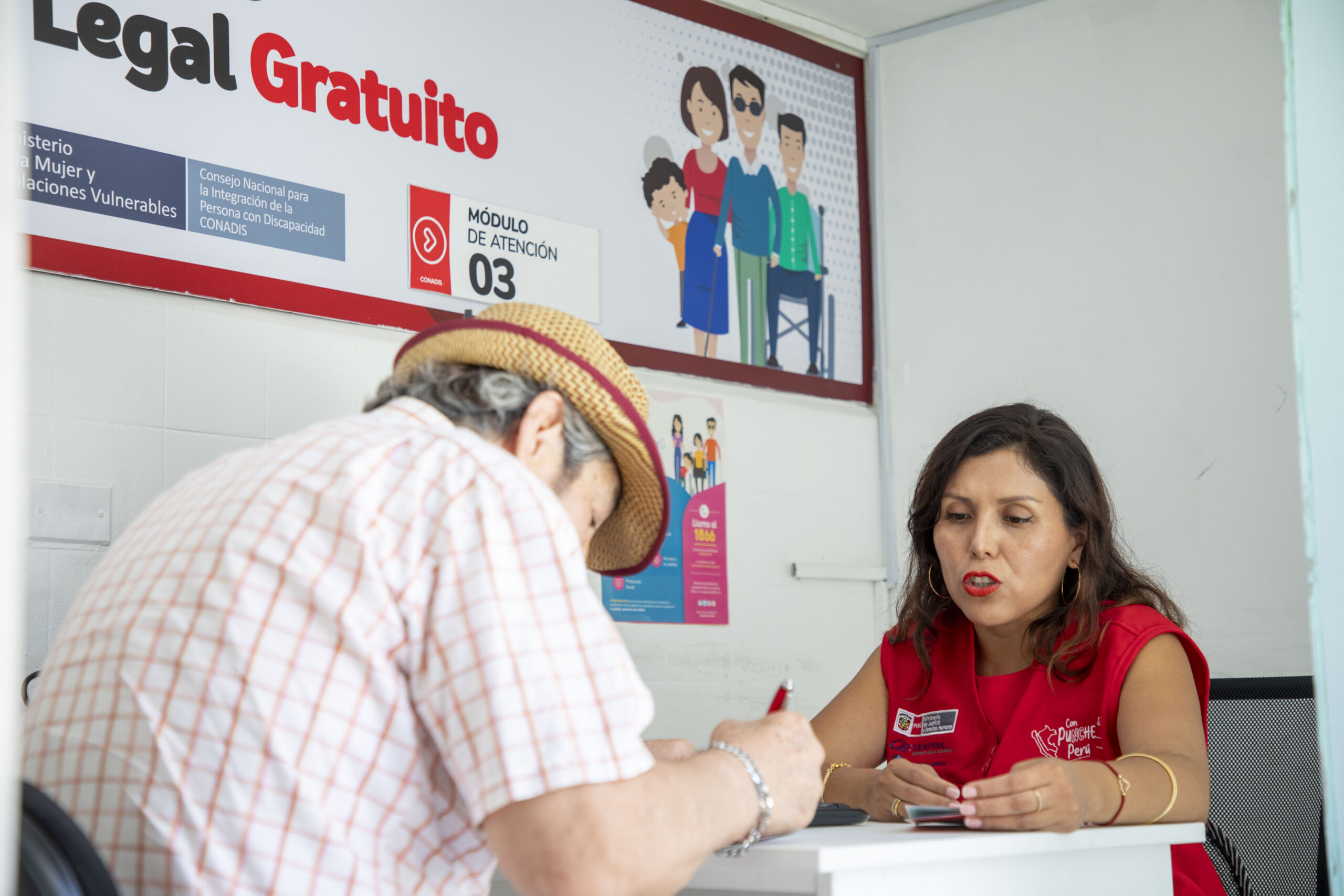 Una funcionaria del MIMP atiende a un adulto mayor en un módulo de asistencia legal gratuita del CONADIS. El hombre firma un documento.