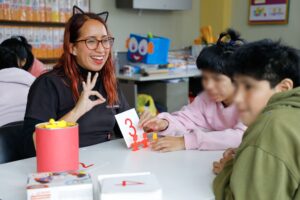 Docente sonriente enseñando el número 3 a varios niños en un aula.