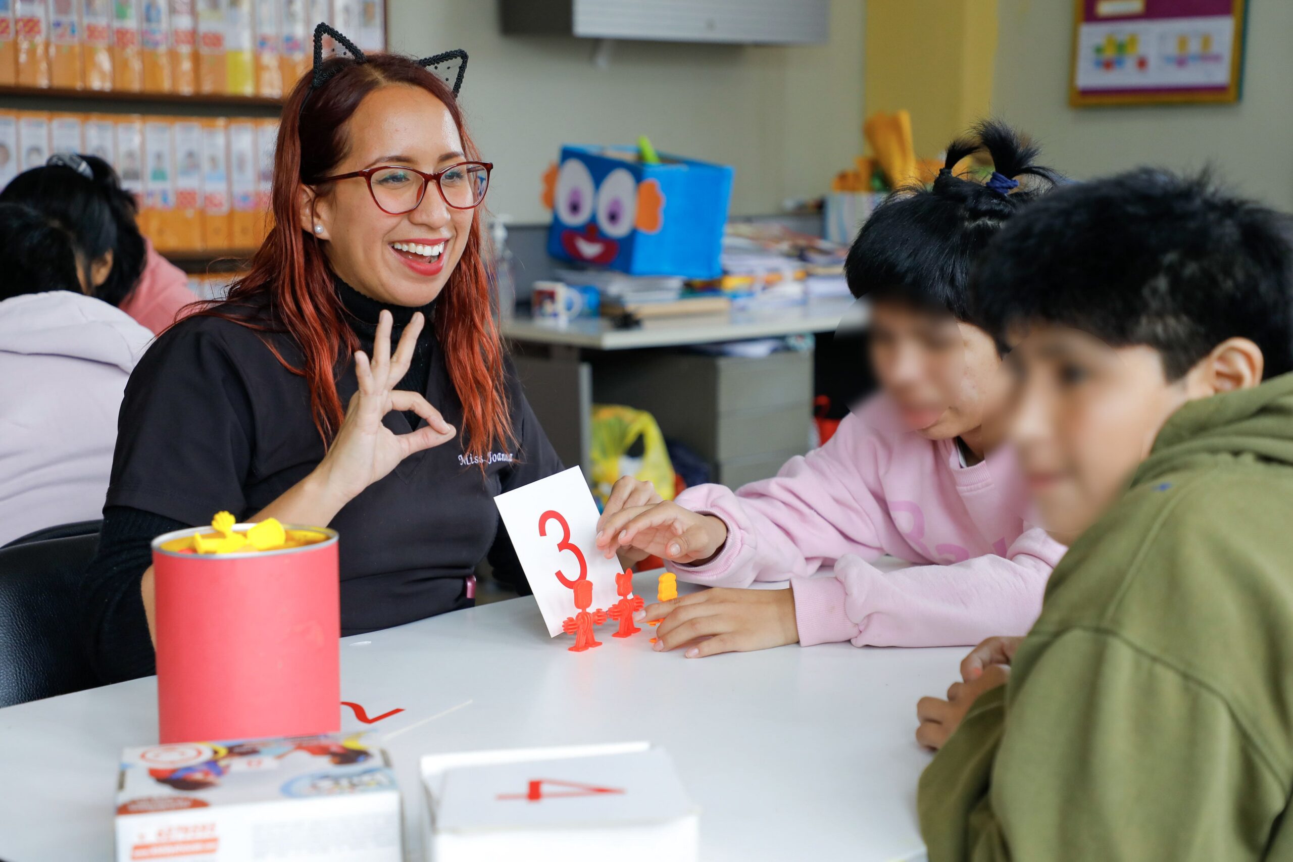 Docente sonriente enseñando el número 3 a varios niños en un aula.