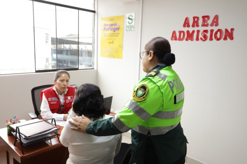 La imagen muestra a una funcionaria pública dando atención a una mujer acompañada de una policía.