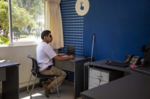 La imagen muestra a una persona con discapacidad visual frente a una computadora portatil.
