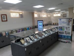 Interior de una biblioteca con vitrinas de libros, una pantalla informativa y un banner de servicios bibliotecarios
