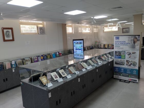 Interior de una biblioteca con vitrinas de libros, una pantalla informativa y un banner de servicios bibliotecarios